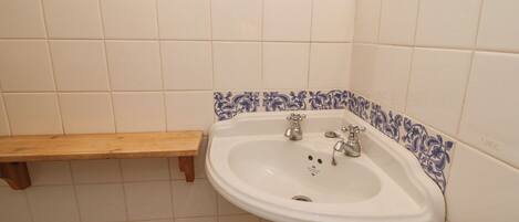 A bathroom with a white sink, two faucets, a wooden shelf, and blue patterned tiles.