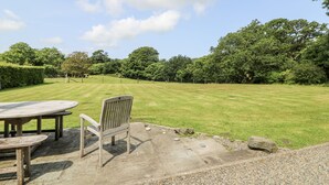 A grassy outdoor area with a picnic table and benches, surrounded by trees and a hedge. - Plas Pontfaen (Fishguard)