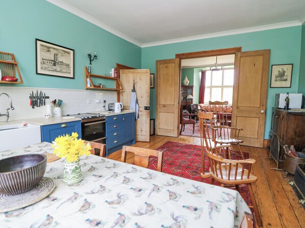 Une cuisine avec des meubles de rangement bleus, une table en bois recouverte d’une nappe à motifs et un tapis rouge.