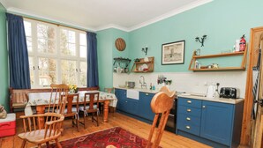 A kitchen with a dining area, featuring a wooden table, chairs, a red patterned rug, and blue cabinets. - Plas Pontfaen (Fishguard)