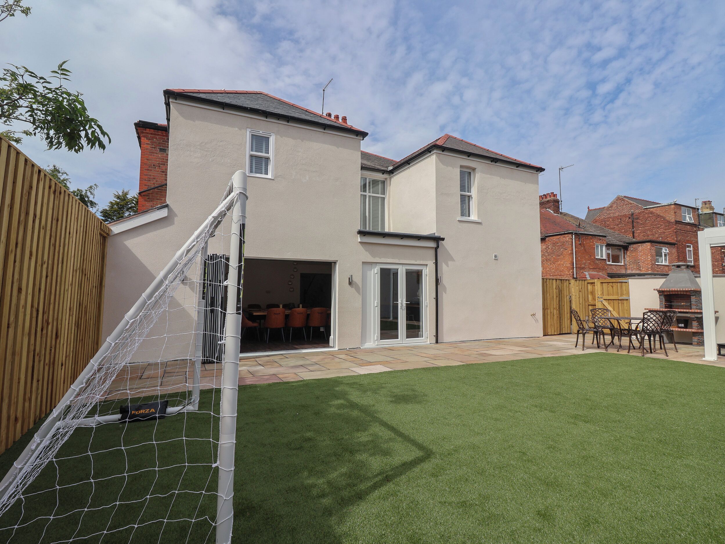 Un patio trasero residencial con terraza, zona de barbacoa y portería de fútbol.