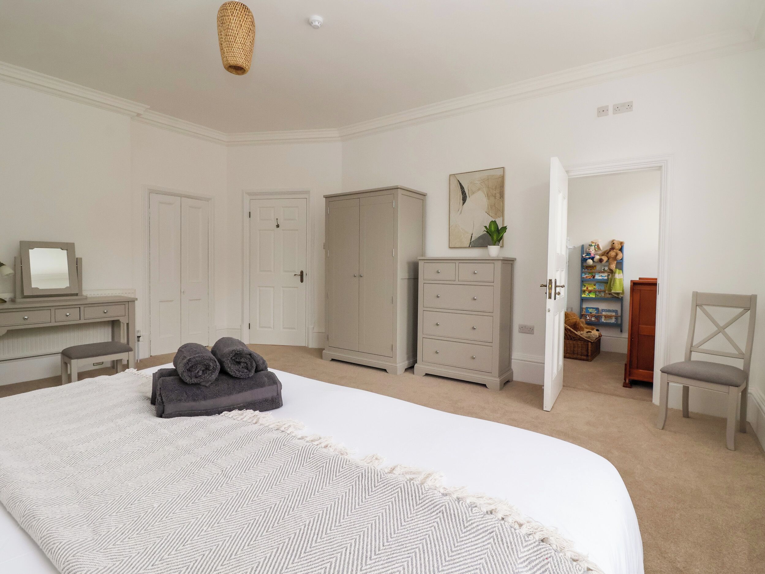 A bedroom with a large bed, a dresser, a wardrobe, a mirror, and a chair.