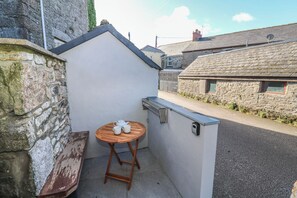 A small, enclosed outdoor area with a wooden table and bench, a white wall, and a stone wall.