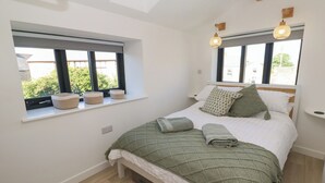 Une chambre à coucher avec un lit, deux fenêtres ornées de jardinières et une table de chevet.
