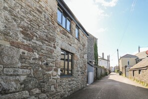 A narrow street with stone buildings, a visible window, and a clear sky.
