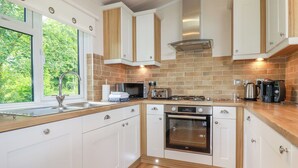 A modern kitchen with white cabinets, a stainless steel oven, a microwave, and a gas stove. - 43 The Maples (St Austell)