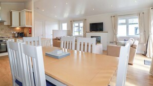 A spacious living area with a dining table, chairs, a sofa, and a television. - 43 The Maples (St Austell)