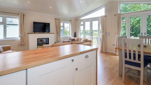 A spacious living area with a wooden dining table, a sofa, and a television mounted on the wall. - 43 The Maples (St Austell)