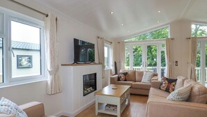 A spacious living room with a fireplace, large windows, and a comfortable seating area. - 43 The Maples (St Austell)