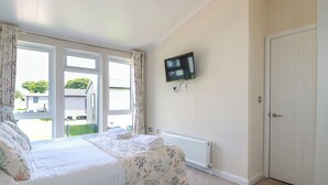 A bedroom with a bed, a TV mounted on the wall, and a door. - 43 The Maples (St Austell)