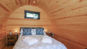 Une pièce chaleureuse aux murs en bois et au plafond vo ûté, avec un lit recouvert d’une courtepointe à motifs, deux oreillers et des lampes de chevet.