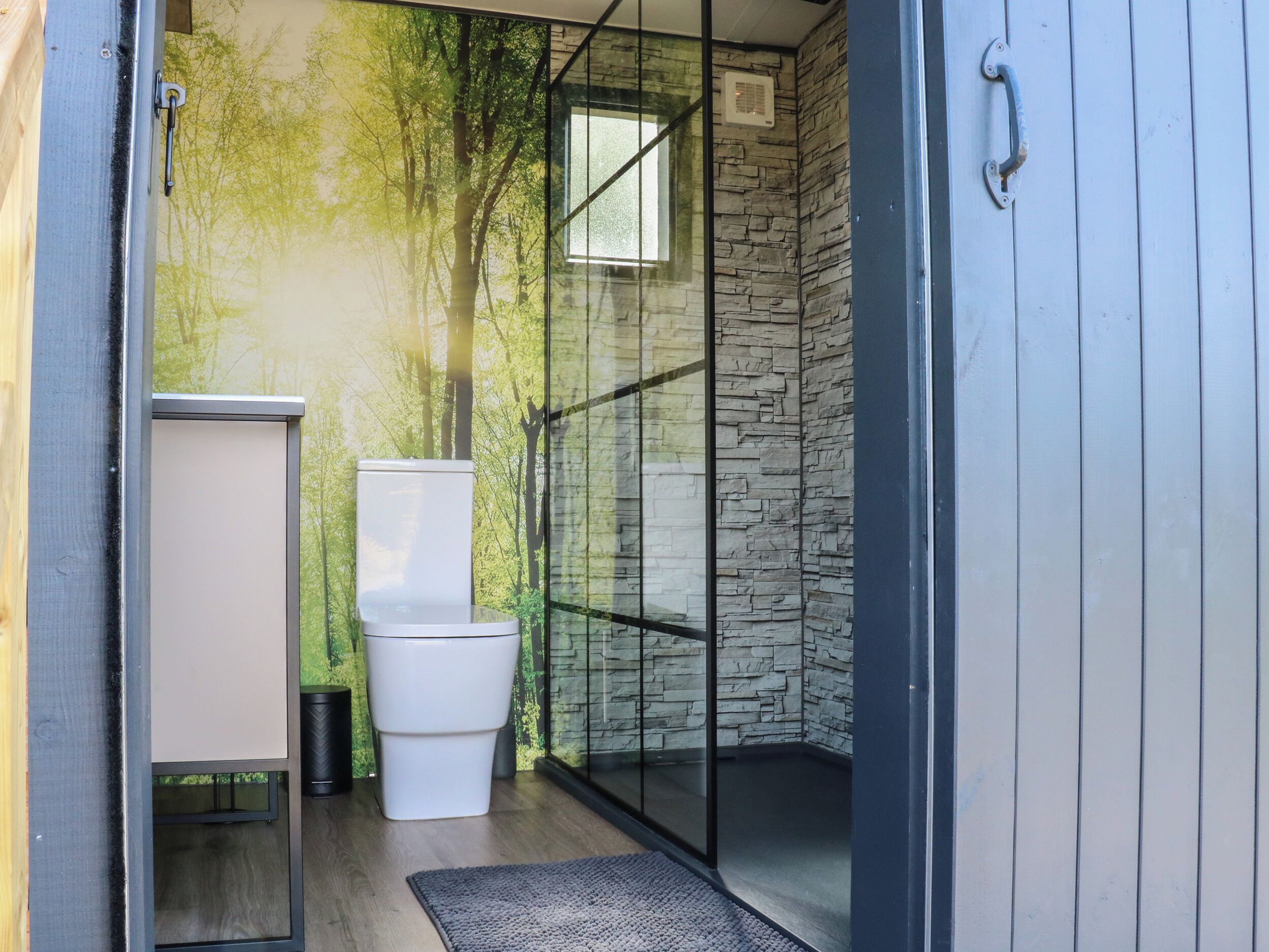 A modern bathroom with a stone wall, a glass shower enclosure, and a white toilet.