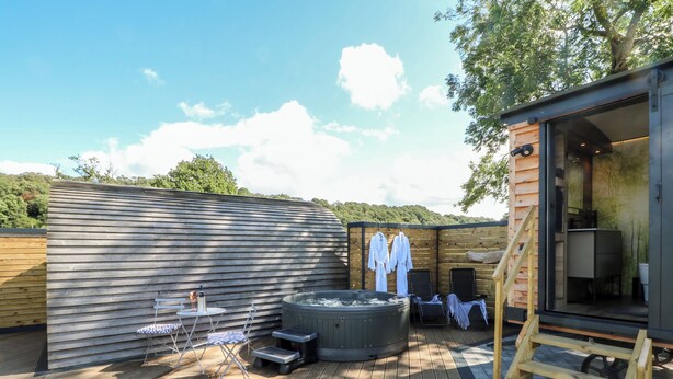 Une terrasse en bois avec un jacuzzi, des chaises longues et une structure de cabane en bois.