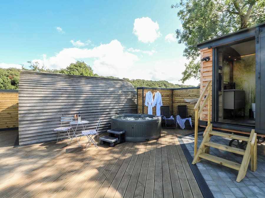 A wooden deck with a hot tub, lounge chairs, and a wooden cabin structure.