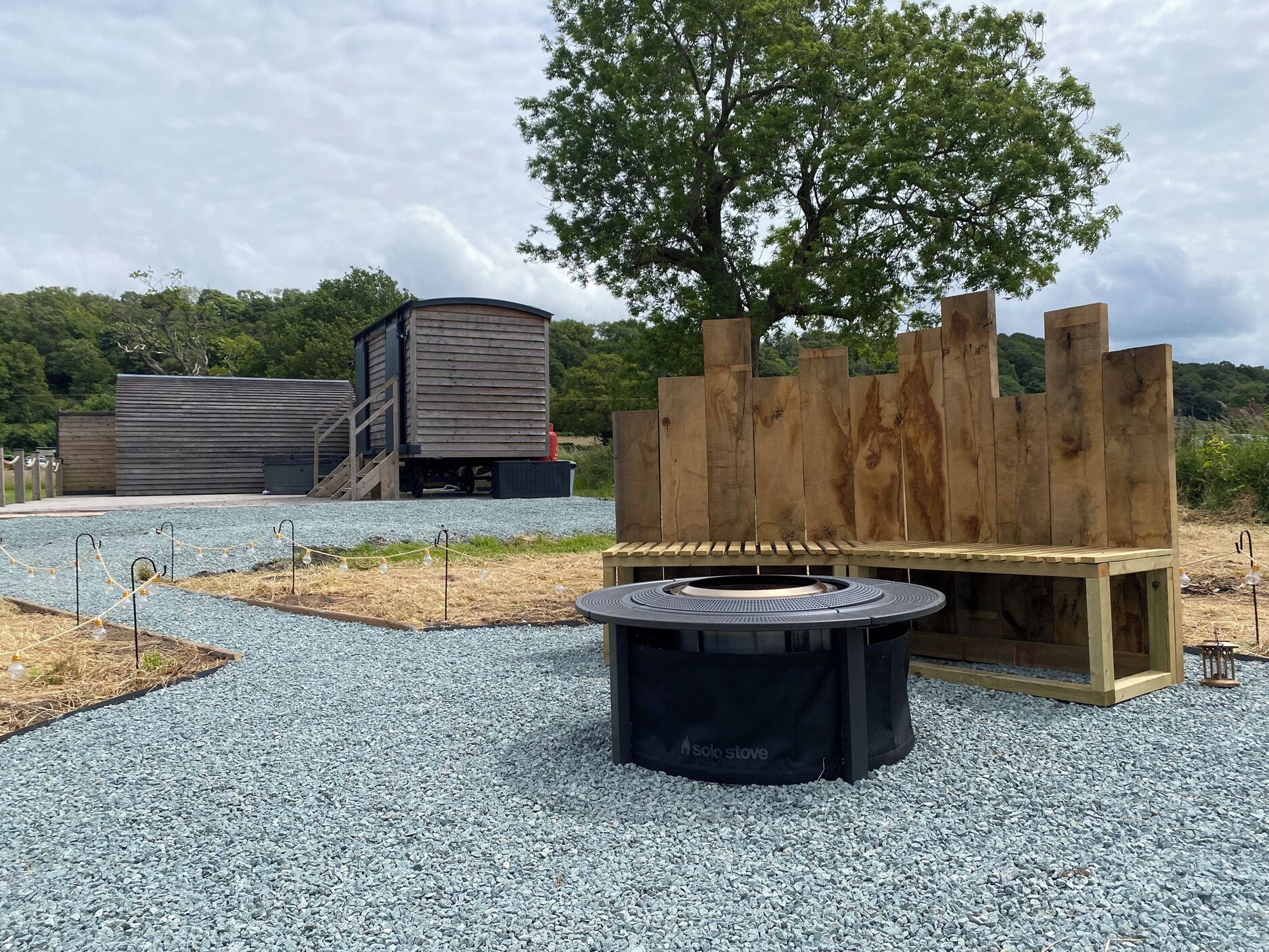 A gravel area with a circular fire pit, wooden benches, and a tree.