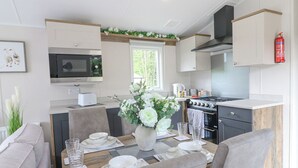Eine moderne Küche mit Mikrowelle, Herd und Spüle. Ein Essbereich mit Tisch für zwei Personen, und ein an der Wand montierter Feuerlöscher.