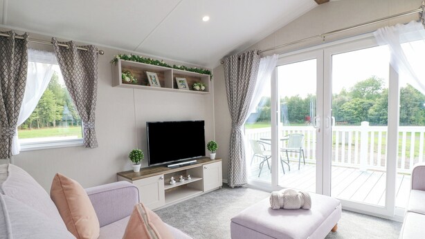 Ein Wohnzimmer mit Sofa, Hocker, Fernseher und einem Balkon mit Stühlen.