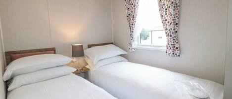 A twin room with two beds, a bedside table with a lamp, and a window with polka dot curtains.