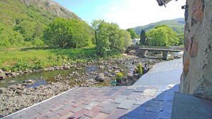 A riverside view with a stone bridge, lush greenery, and a paved walkway. - Riverbank Cottage (Caernarfon)