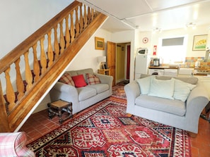 A living room with a staircase, a sofa, a patterned rug, and a kitchen area with appliances.
