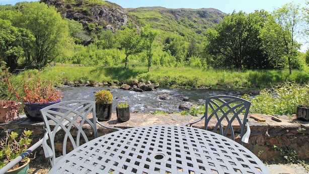 A table and chairs in a garden with a view of a river and hills. - Riverbank Cottage (Caernarfon)