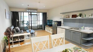 A modern living room with a sofa, coffee table, and a dining area with a table and chairs. There is a kitchen area with a sink and countertop. - Matt & Co. Group (Bangkok)