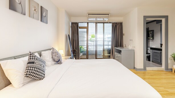 A modern hotel room with a large bed, a desk, and a sliding glass door to a balcony. - Matt & Co. Group (Bangkok)