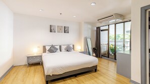 A modern bedroom with a large bed, bedside tables, a mirror, and a view through a sliding glass door. - Matt & Co. Group (Bangkok)