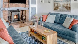 A living room with a fireplace, a sofa, a coffee table, and a television mounted on the wall. - The Cubby Hole (Penzance)