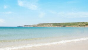 A beach with clear water, a sandy shore, and a distant rocky coastline under a clear sky. - The Cubby Hole (Penzance)
