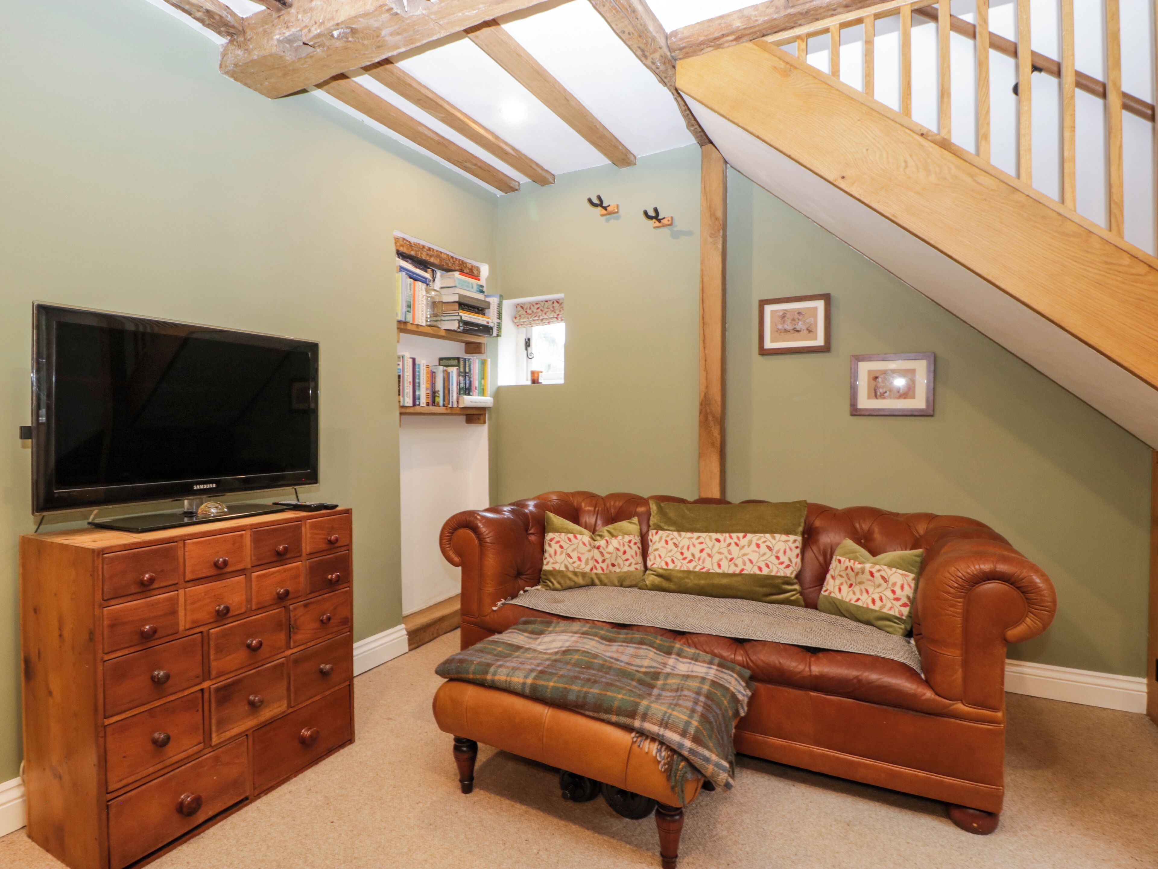 Una sala de estar acogedora con un sofá de cuero, un mueble bajo de televisión de madera y una escalera.