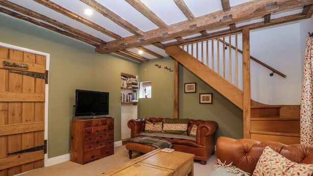 A cozy living room with a wooden staircase, a television, a leather sofa, and a bookshelf. - 2 Loxter Villas (Ledbury)