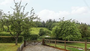 A paved pathway leading to a wooden gate, surrounded by lush greenery and trees. - 2 Loxter Villas (Ledbury)
