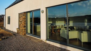 Une maison moderne avec une façade en pierre, de grandes portes-fenêtres coulissantes et une vue sur un espace de salle à manger intérieur.