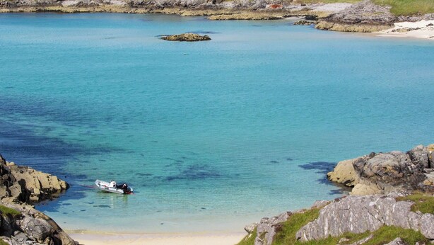 Un paysage côtier avec une mer bleue et limpide, des rivages rocheux et un petit bateau ancré près de la plage.