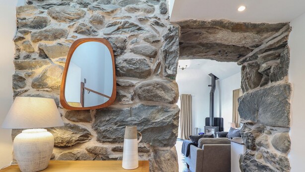 A stone-walled room with a wooden dresser, a mirror, and a lamp. - Gaerau Bach (Llanbedr)