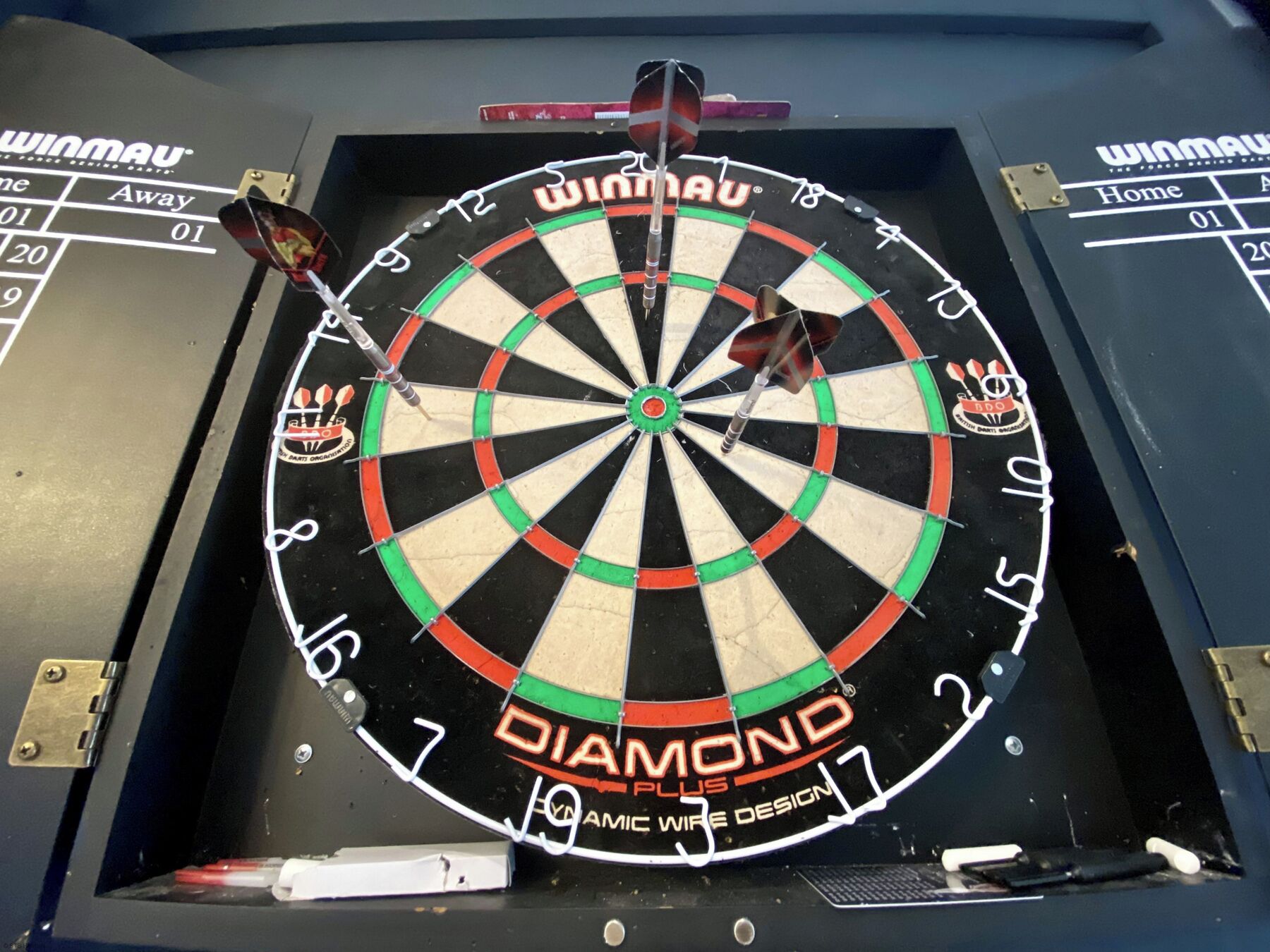 Un dardo con el nombre de marca 'WINMAU' y 'DIAMOND PLUS' visibles, que indica un diseño especializado para dardos.