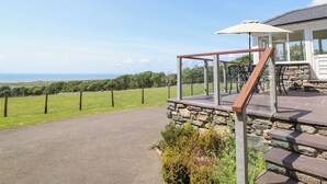 Un patio con un muro de piedra, barandilla de vidrio y vista al océano.