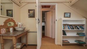 Ein gemütliches Zimmer mit einem Holztisch, einem Bücherregal, einem Spiegel und einer Tür zu einem anderen Raum.
