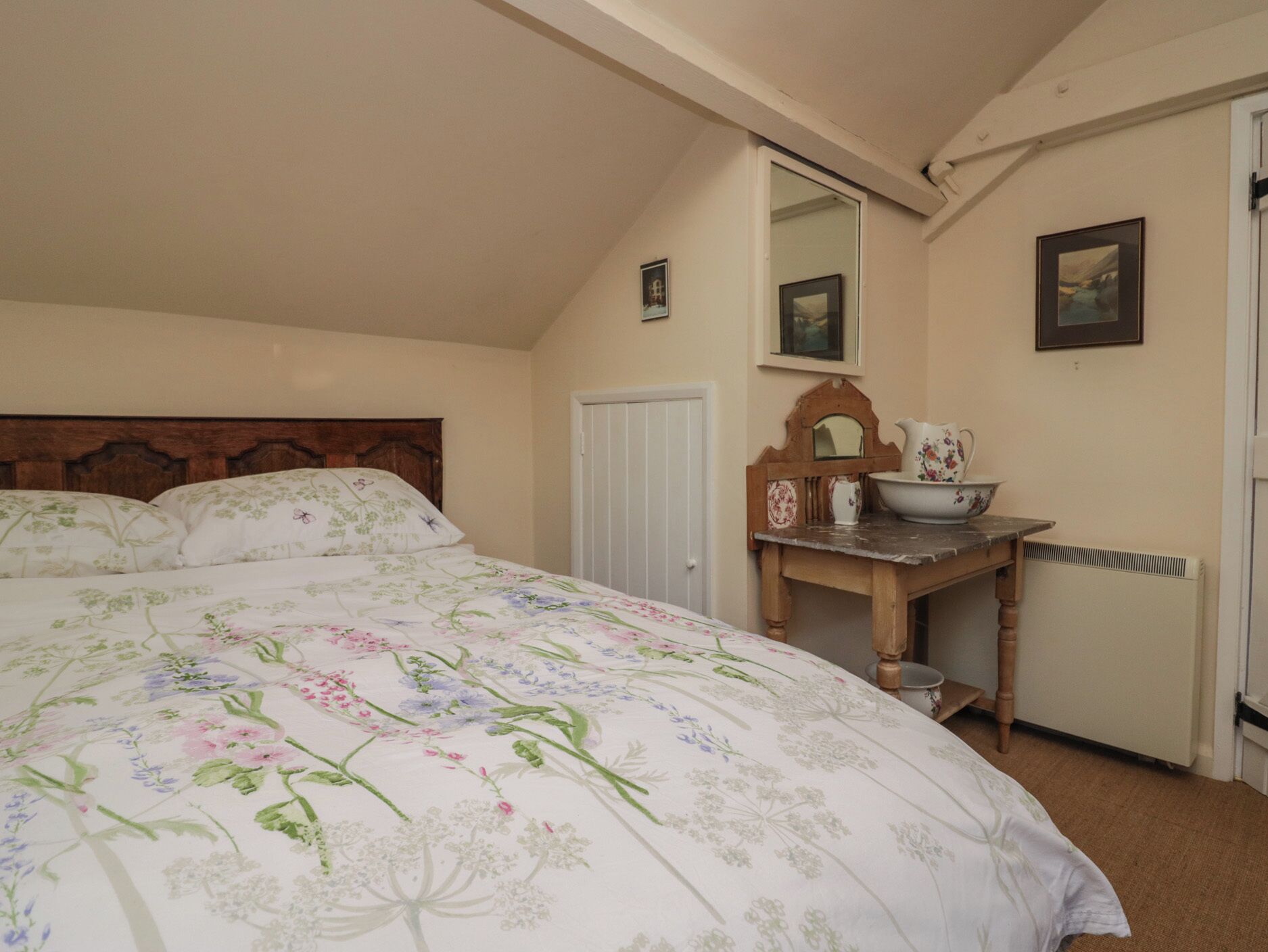 Een slaapkamer met een groot bed, een houten dressoir, een spiegel en een radiator.