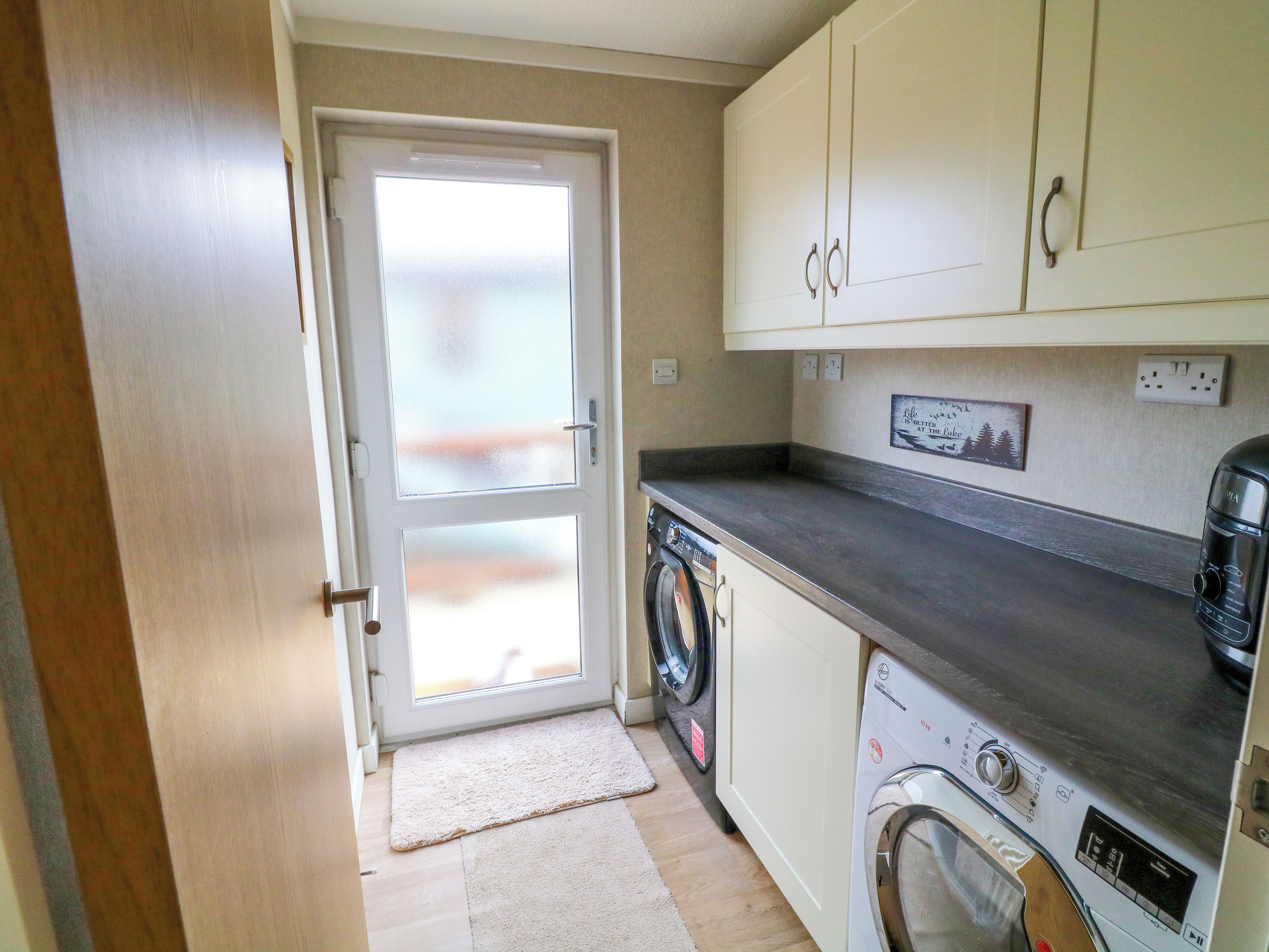 A compact kitchen with a washing machine, a coffee maker, and a door leading to a balcony.