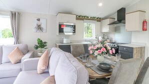 A modern kitchen with a microwave, stove, and sink. There is a dining area with a table and chairs, and a living room with a sofa and cushions.