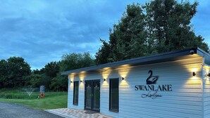 A small, light blue building with a swan logo and the name 'SWAN LAKE Lodge' on the front. It has two doors and a small porch area.