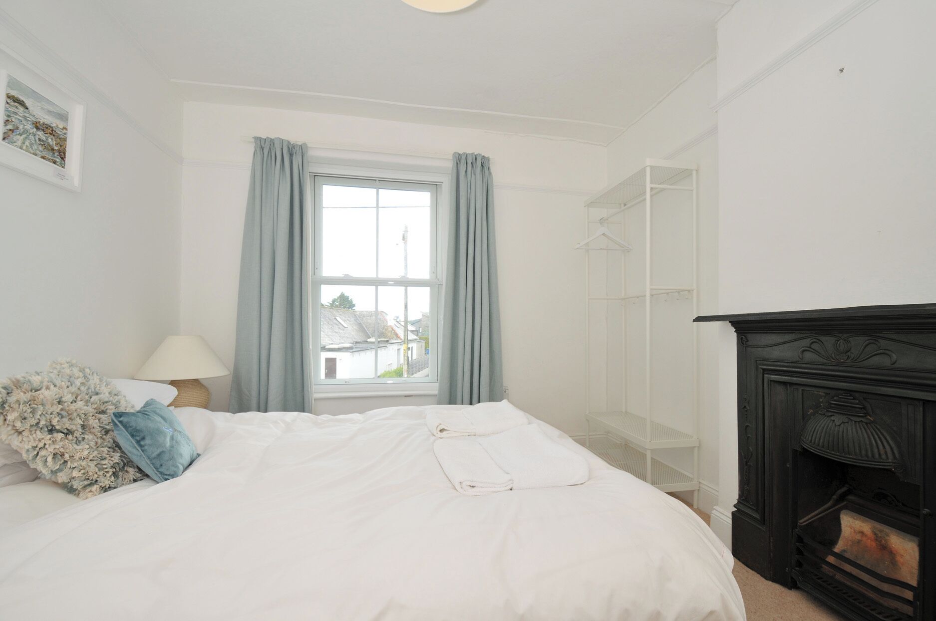 Um quarto com cama, janela com cortinas, luminária, guarda-roupa branco e lareira preta.