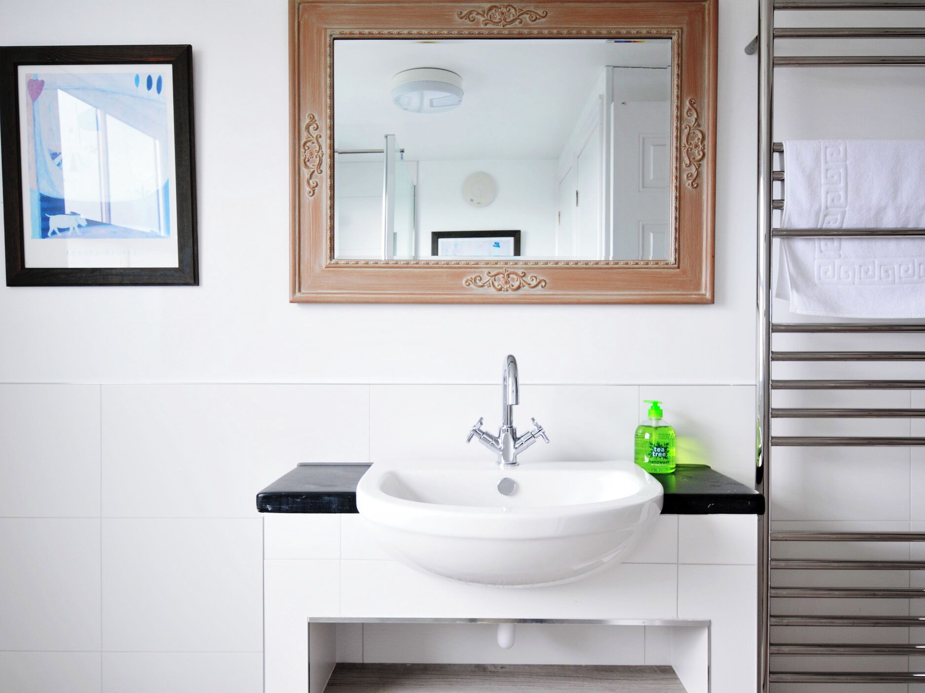 Un baño con un lavamanos blanco, un espejo con un marco decorado y un perchero con una toalla blanca.