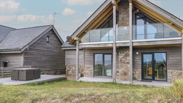 Une maison moderne à deux étages, dotée d’une façade en pierre, de grandes fenêtres et d’un balcon.