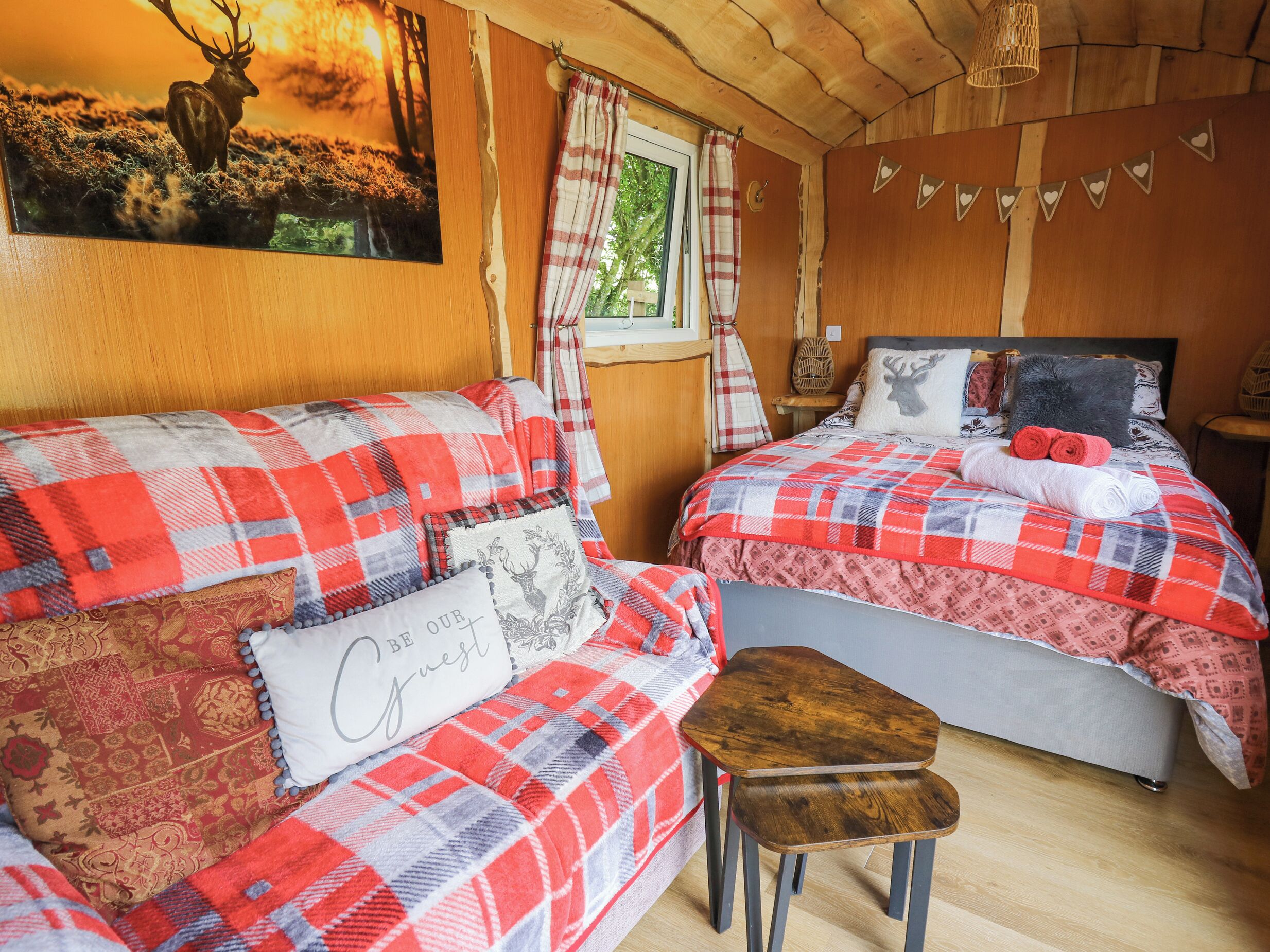 Een gezellig houten huisje met twee bedden, een tafeltje en een raam met gordijnen.