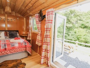 A cozy room with a bed, a window with curtains, a wooden ceiling, and a view of greenery outside. - Shepherd's Cwtch (Llandovery)