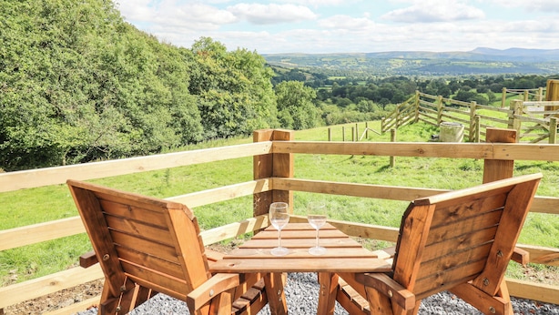 Terraza de madera con mesa y sillas que da a un paisaje pintoresco.