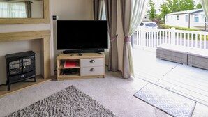 Ein Zimmer mit Fernseher auf Holzständer, einem kleinen Schrank, einem Teppich und Blick auf einen weißen Zaun und Grünfläche draußen.